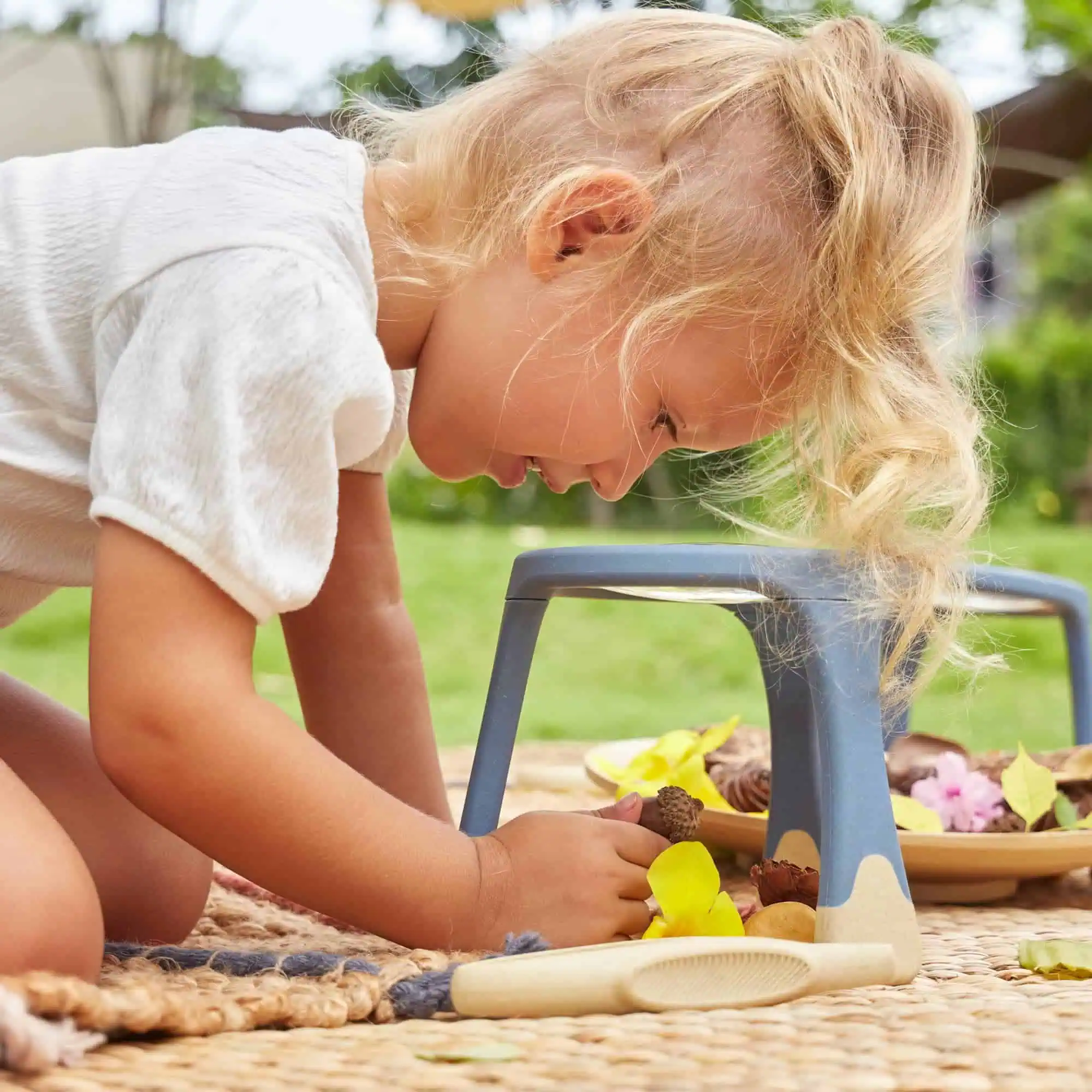 Farbenfrohe kleine Kind spielt draußen im Garten, auf einer kuscheligen Decke mit Spielzeug und Naturmaterialien, schöne Sommerzeit.